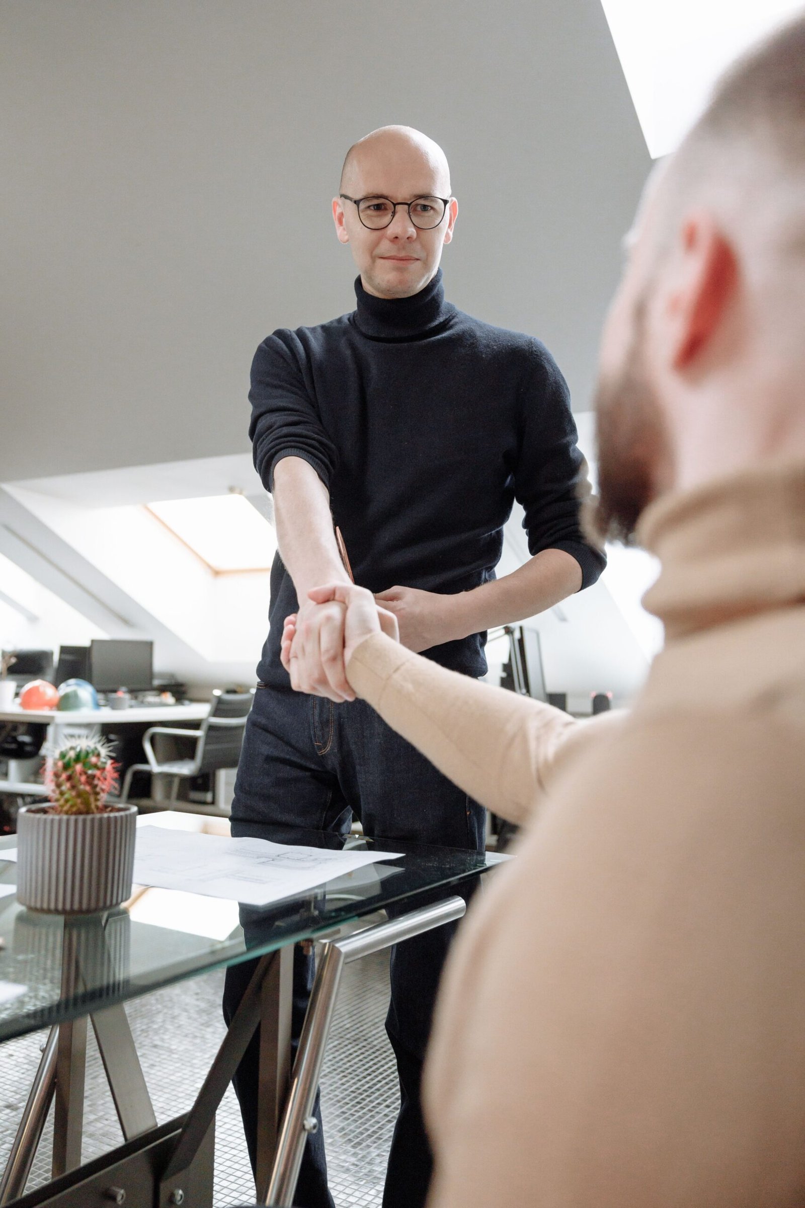 Two professionals shaking hands in a modern coworking space, symbolizing collaboration.